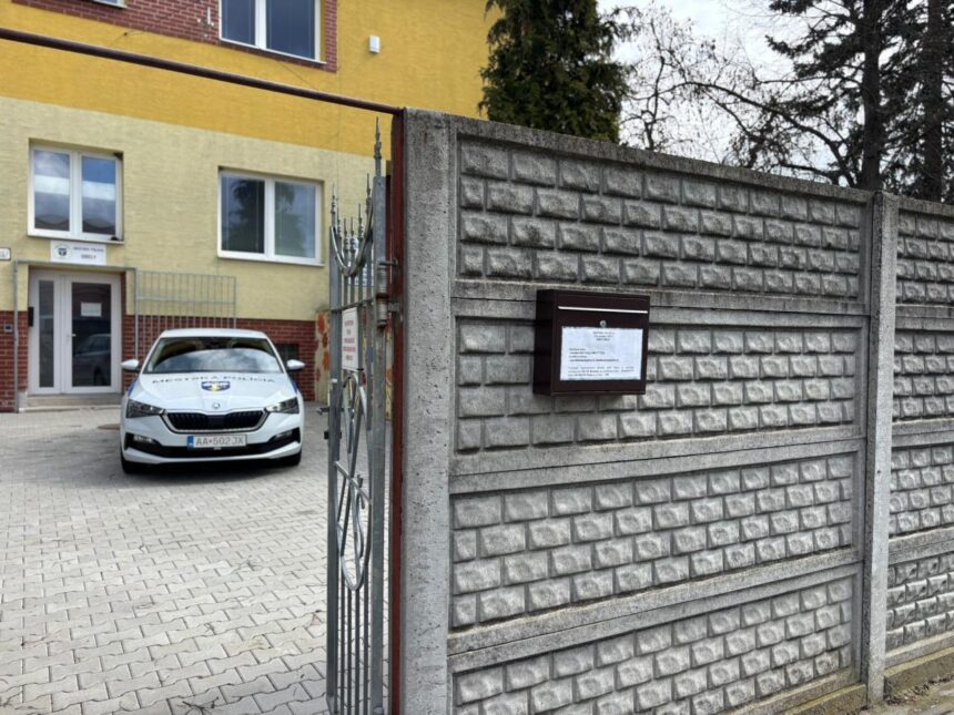 Brána s nápisom Mestská polícia a policajné auto zaparkované pred budovou mestskej polície v Gbeloch.
