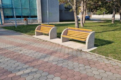 Dve nové lavičky umiestnené na chodníku pred budovou Domu kultúry v Gbeloch, v pozadí sú stromy a parkovisko.