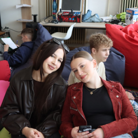 Dve ženy sediace na vankúšoch počas diskusie v mládežníckej klubovni KiviK, v pozadí ďalší mladí ľudia.