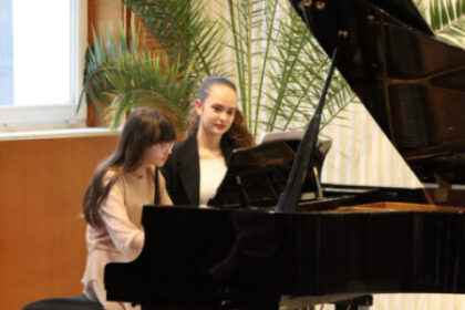 Ilustrácia dvoch mladých dievčat hrajúcich na klavíri počas kultúrneho podujatia v Senici.