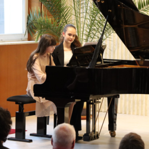 Ilustrácia dvoch mladých dievčat hrajúcich na klavíri počas kultúrneho podujatia v Senici.