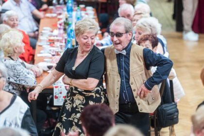 Muž a žena tancujúci na podujatí Medzinárodného dňa žien v Skalici, v pozadí ďalší účastníci pri stole.