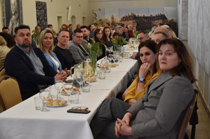 Skupina ľudí sediacich pri stole na slávnostnom stretnutí v Kultúrno-osvetovom centre v Holíči pri odovzdávaní dotácií miestnym organizáciám.