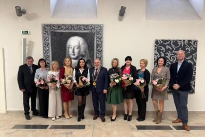 Skupina pedagógov držiacich kvety počas slávnostného stretnutia pri príležitosti Dňa učiteľov v Holíči, v pozadí obraz muža.