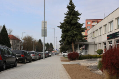 Ulica v Senici s novými chodníkmi a stromami, viditeľné parkovacie miesta a zeleň pozdĺž cesty.