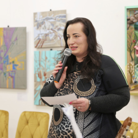 Žena hovorí do mikrofónu počas literárneho večera v Záhorskom osvetovom stredisku, v pozadí sú obrazy na stene.