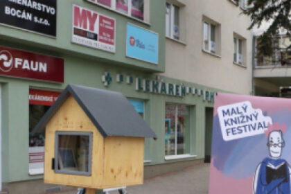 Fotografia knižnej búdky na Námestí oslobodenia v Senici počas Malého knižného festivalu s knihami a plagátom podujatia.