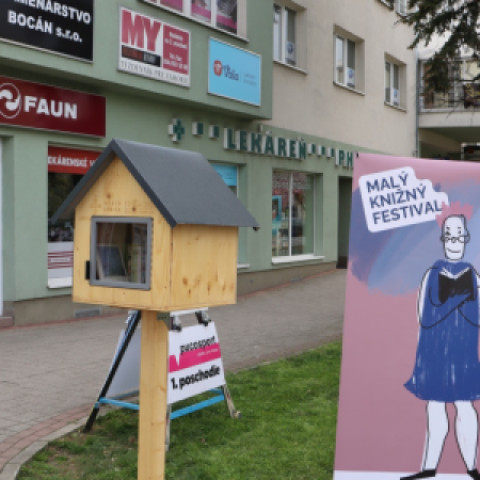 Fotografia knižnej búdky na Námestí oslobodenia v Senici počas Malého knižného festivalu s knihami a plagátom podujatia.