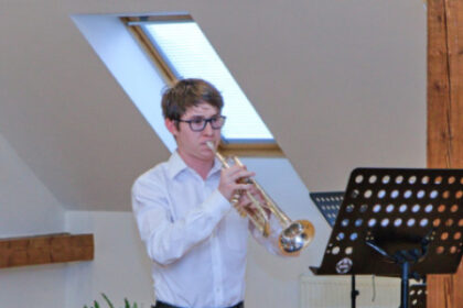 Mladý muž v bielej košeli a čiernych nohaviciach hrá na trúbke počas koncertu senických hudobníkov vo Veľkých Pavloviciach.