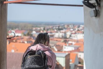 Osoba s batohom stojaca a pozerajúca sa na panorámu mesta Skalica z výšky počas tematickej prehliadky.