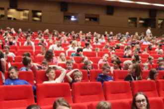 Skupina dievčat sedí na červenej sedačke v sále počas eko-muzikálu v Senici, v pozadí sú ďalší diváci.