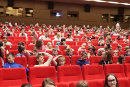 Skupina dievčat sedí na červenej sedačke v sále počas eko-muzikálu v Senici, v pozadí sú ďalší diváci.