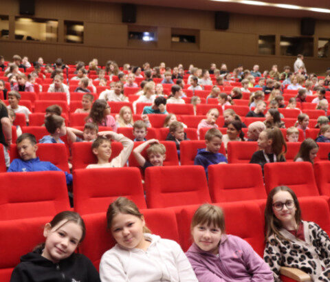 Skupina dievčat sedí na červenej sedačke v sále počas eko-muzikálu v Senici, v pozadí sú ďalší diváci.