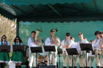 Skupina hudobníkov v tradičných krojoch hrá na nástrojoch počas slávnosti stavania mája na námestí v Senici.