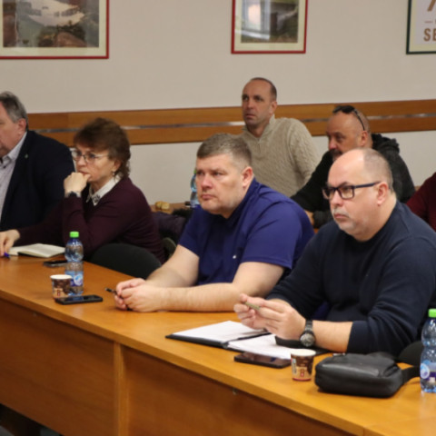 Skupina starostov a starostiek okresu Senica sediacich pri stole počas pracovného stretnutia, diskutujúcich o bezpečnosti a sociálnych službách.