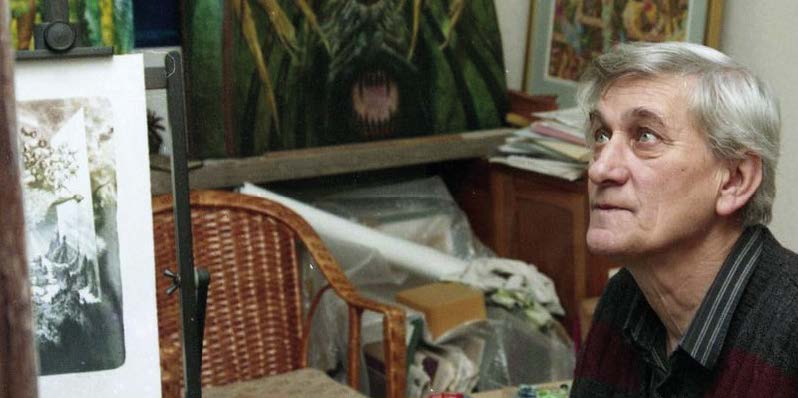 Starší muž sediaci pri stole s vystaveným obrazom, v pozadí ďalšie umelecké diela.