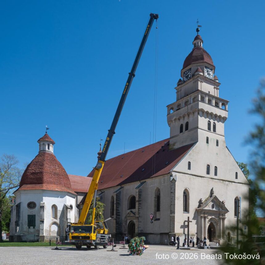 Budova s vežou a žeriav zdvíhajúci tradičný zdobený máj na Námestí slobody v Skalici počas kultúrneho podujatia.