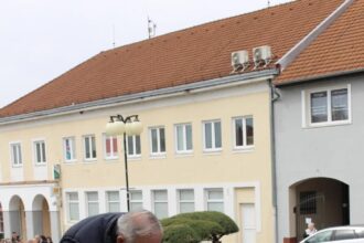 Muž kladie veniec s modrými a červenými kvetmi a páskou s nápisom MESTO na pamätník padlých vojakov na Námestí mieru v Holíči počas pietneho aktu.