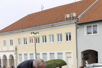 Muž kladie veniec s modrými a červenými kvetmi a páskou s nápisom MESTO na pamätník padlých vojakov na Námestí mieru v Holíči počas pietneho aktu.