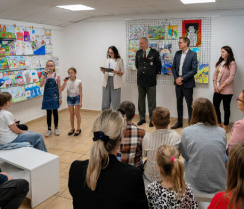 Skupina detí a dospelých na vernisáži výtvarnej súťaže v Záhorskom osvetovom stredisku v Senici, detské výtvarné diela vystavené na stenách.