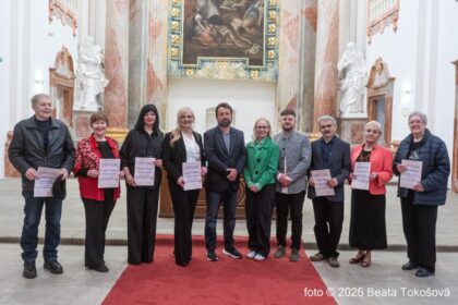 Skupina ľudí oblečených formálne drží diplomy na vernisáži výstavy Skalická paleta 2026, v pozadí sú viditeľné umelecké diela.