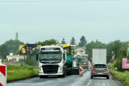 Cesta I/51 medzi Senicou a Rohovom počas opravy s nákladnými autami, osobným vozidlom, dopravnými značkami a bariérami, na povrchu čerstvý asfalt.