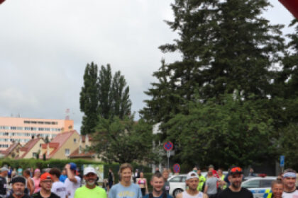 Skupina bežcov pred štartovacím oblúkom Záhoráckeho maratónu v Senici, všetci v športovom oblečení so štartovnými číslami, v pozadí budovy a stromy.
