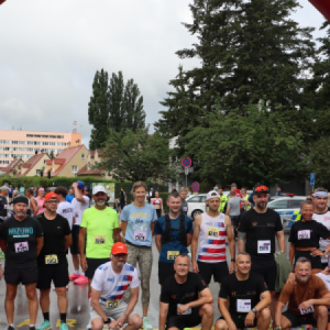 Skupina bežcov pred štartovacím oblúkom Záhoráckeho maratónu v Senici, všetci v športovom oblečení so štartovnými číslami, v pozadí budovy a stromy.
