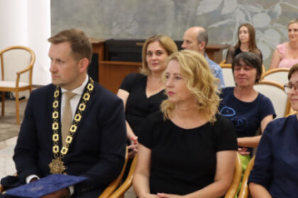 Skupina ľudí sediacich v obradnej sieni mestského úradu v Senici, medzi nimi muž v obleku s reťazou na krku, pri príležitosti oceňovania mnohonásobných darcov krvi.