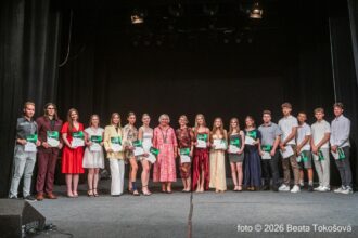 Skupina mladých ľudí na pódiu v Dome kultúry v Skalici počas slávnostného oceňovania najlepších absolventov škôl, držia ocenenia a usmievajú sa.