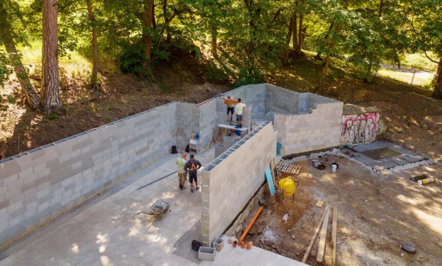 Stavebné práce na výstavbe muriva v lesoparku Hájek v Skalici, vidieť pracovníkov a stavebné materiály na stavenisku.