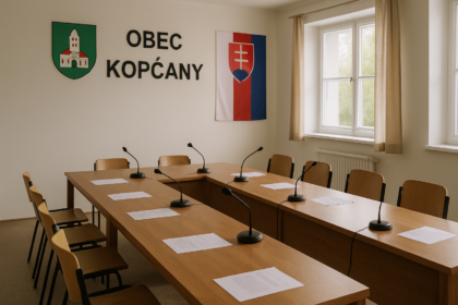 Zasadacia miestnosť obecného úradu v Kopčanoch pripravená na zasadnutie obecného zastupiteľstva s dreveným stolom, stoličkami, papiermi a mikrofónmi, slovenskou vlajkou v pozadí.