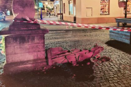 Zničená socha sv. Floriána ležiaca na zemi v centre Skalice, obklopená červenobielym pásmom, v pozadí vidieť budovy a pouličné osvetlenie.