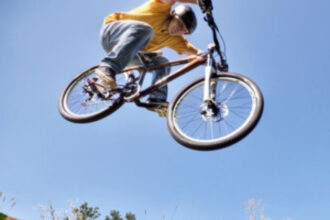 Chlapec na bicykli skáče cez prekážku na modrom pozadí s oblohou a zeleňou, ilustrujúci bikepark pre mladých v Senici.