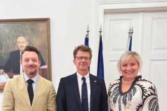 Traja ľudia v interiéri pri vlajkách a portréte na stene