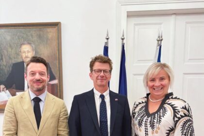 Traja ľudia v interiéri pri vlajkách a portréte na stene