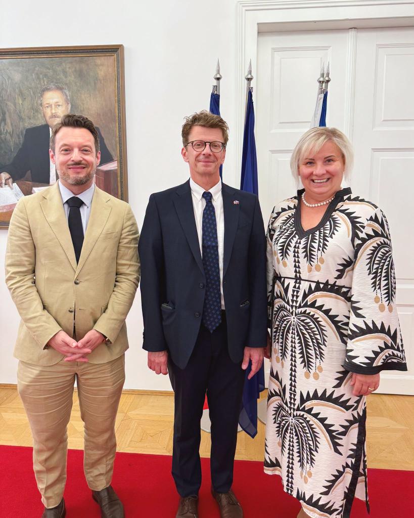 Traja ľudia v interiéri pri vlajkách a portréte na stene
