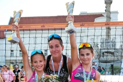 Mladé volejbalistky na stupni víťazov s trofejami a kvetmi po plážovom turnaji.