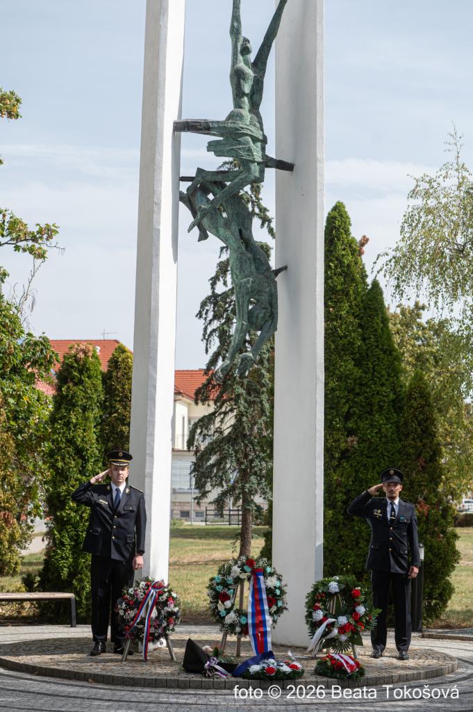 Pamätník s vencami a dvoma uniformovanými osobami pri pietnom akte v Skalici.