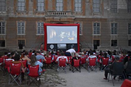 Vonkajšie filmové premietanie pred historickou budovou s publikom na stoličkách a veľkým plátnom.