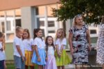 Deti a dospelá osoba pred budovou školy na začiatku školského roka.
