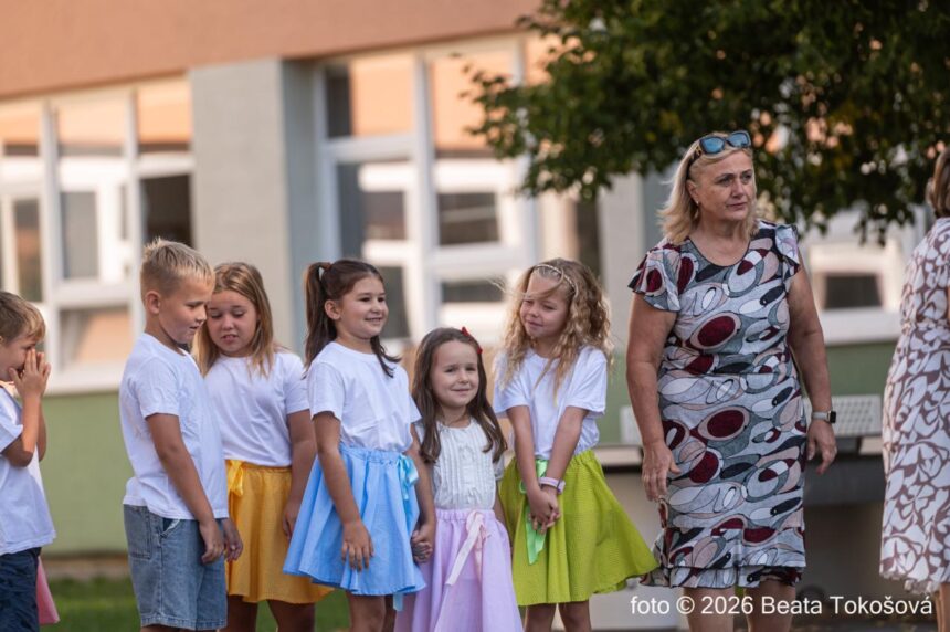 Deti a dospelá osoba pred budovou školy na začiatku školského roka.