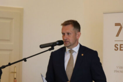 Osoba hovorí pri mikrofóne na pietnom podujatí v sále.