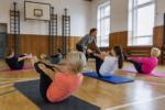 Skupina dospelých cvičí pilates v školskej telocvični.
