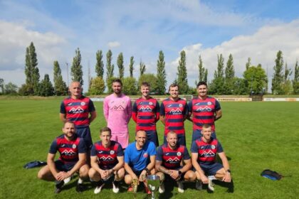 Skupina futbalistov na ihrisku s trofejami.