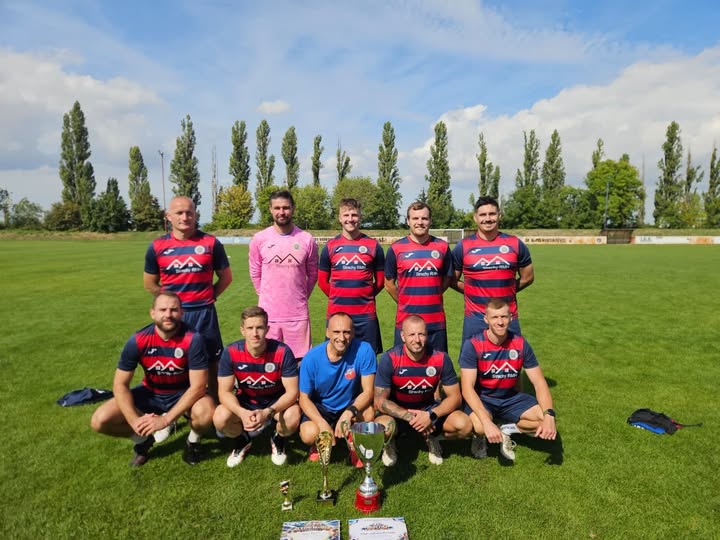 Skupina futbalistov na ihrisku s trofejami.