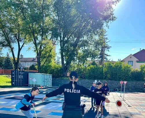 Deti na dopravnom ihrisku s policajtom počas výučby pravidiel cestnej premávky.