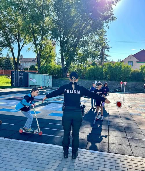 Deti na dopravnom ihrisku s policajtom počas výučby pravidiel cestnej premávky.