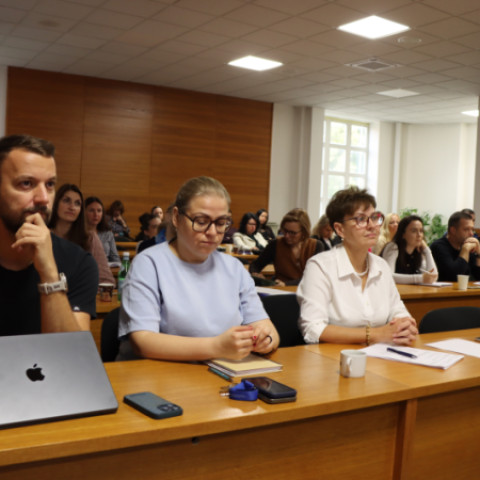 Účastníci seminára sedia v zasadačke pri stole s notebookom a poznámkami.