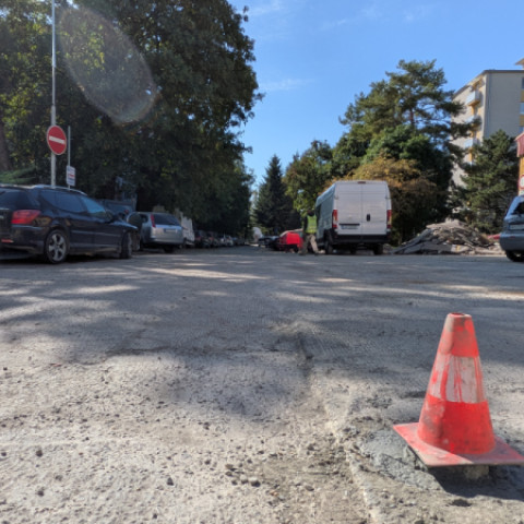 Ulica v Senici s odstavenými autami, dodávkou, dopravným kužeľom a prebiehajúcimi prácami na ceste.